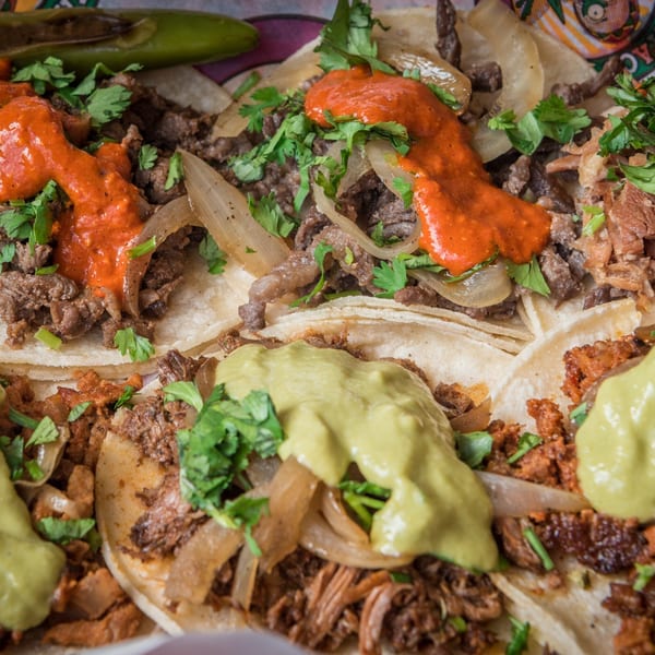 Close-up of Guanataco's Mexican tacos with various meats, red and green sauces, onions, and cilantro.