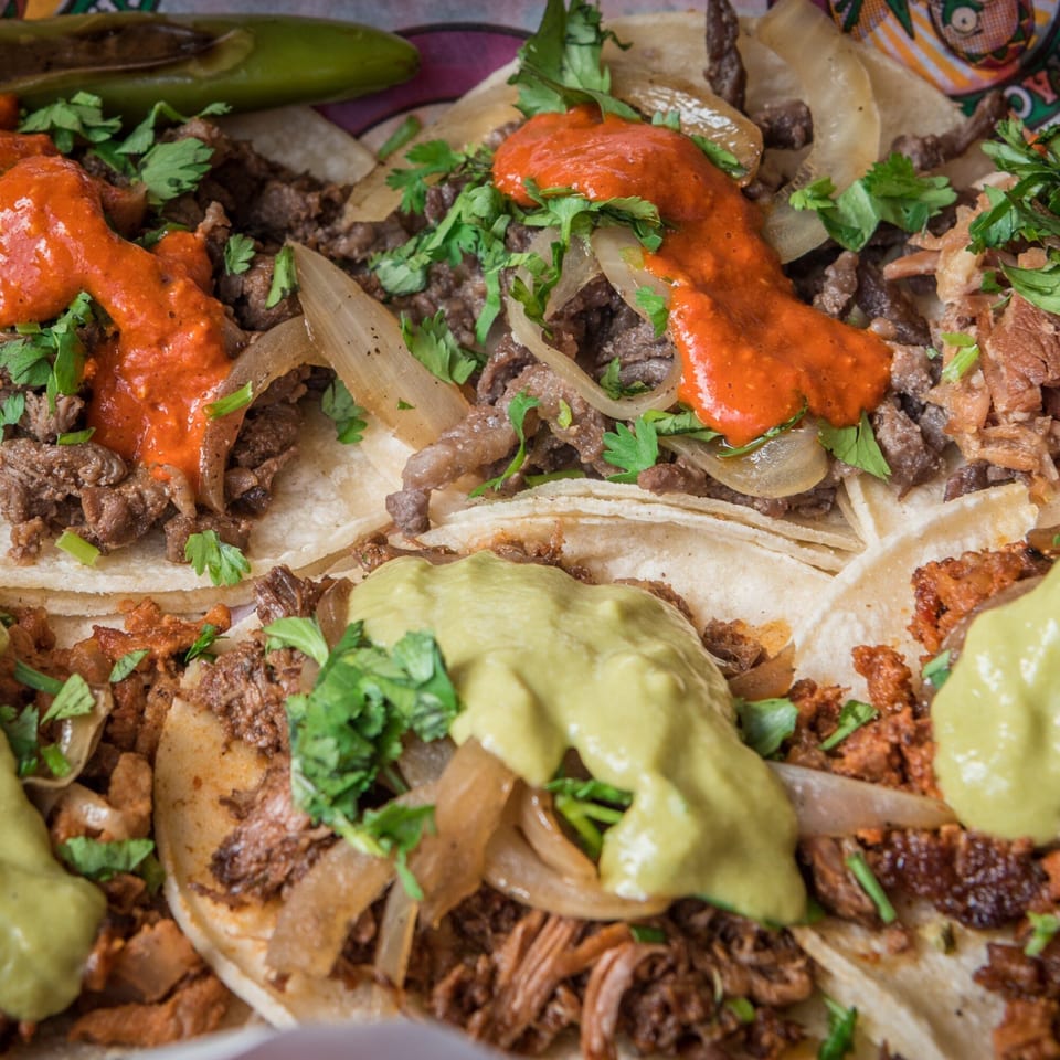 Close-up of Guanataco's Mexican tacos with various meats, red and green sauces, onions, and cilantro.