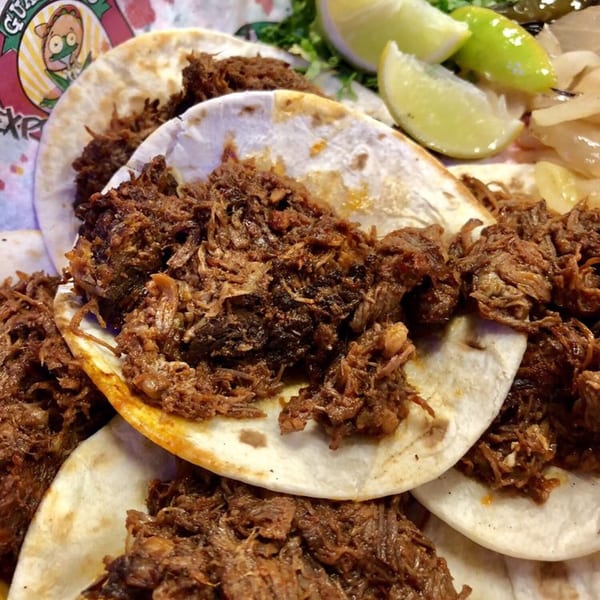Close-up of Guanataco's shredded beef tacos with lime wedges and pickled onions.