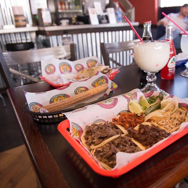 A table at Guanataco with a tray of tacos, a churro, and a white beverage.