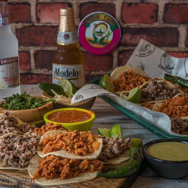 Assortment of Guanataco tacos with various fillings, salsas, cilantro, limes, and bottled drinks.