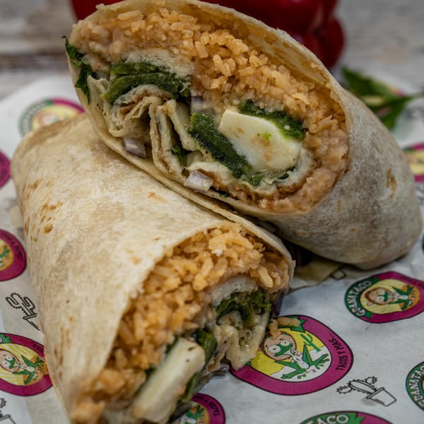 Two Guanataco burritos, one cut in half, revealing rice, green chiles, and cheese on branded paper.