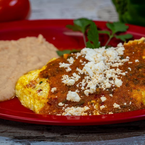 Guanataco's Mexican omelet with red sauce, crumbled cheese, and refried beans on a red plate.