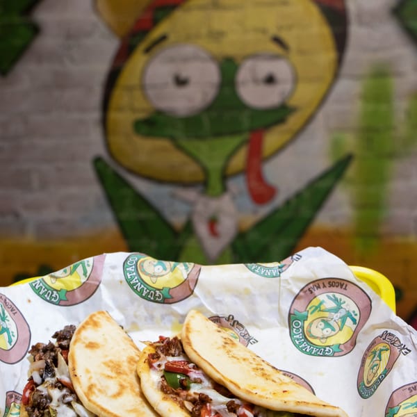 Guanataco's tacos with melted cheese, meat, and vegetables in a branded paper-lined basket.