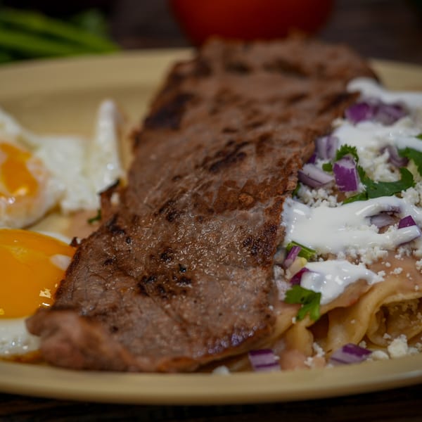 Guanataco's carne asada with two fried eggs, chilaquiles, sour cream, cheese, and red onions.