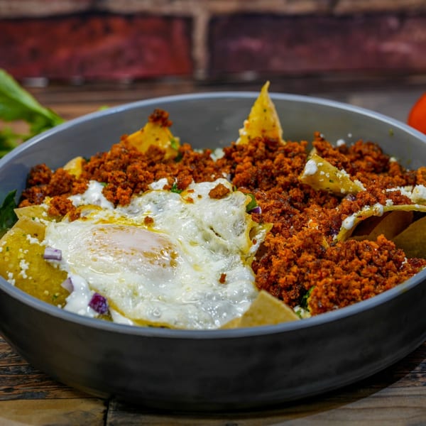 Chilaquiles with green sauce, chorizo, and a fried egg in a gray bowl on a wooden table.