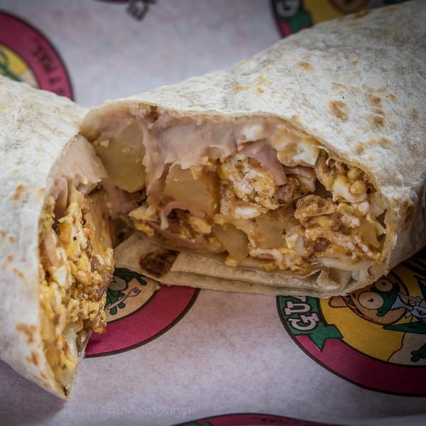 A Guanataco breakfast burrito, cut in half, revealing scrambled eggs and potatoes inside a tortilla.